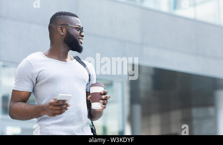 Junge afrikanische Mann mit Telefon und Kaffee zu genießen Tag gehen Stockfoto