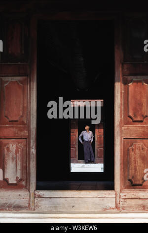 Mandalay, Myanmar - April 2019: burmesische Mann in longyi Rock im Königlichen Palast Eingang. Rahmung mit einem hölzernen Arch, vertikale Ausrichtung Stockfoto