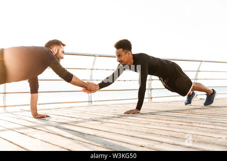 Zwei attraktive selbstbewussten jungen gesunden Sportler im Freien am Strand, Training zusammen, Push-ups Stockfoto