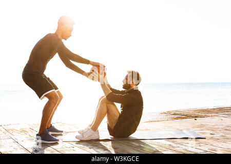 Zwei attraktive junge gesunde Sportler im Freien am Strand, Training, Übungen mit einer schweren Kugel Stockfoto