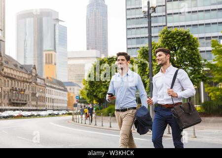 Bild von einem zufrieden lächelnden Jungen zwei Freunde und Kollegen business men Walking im Freien neben der Suche mit Telefon. Stockfoto