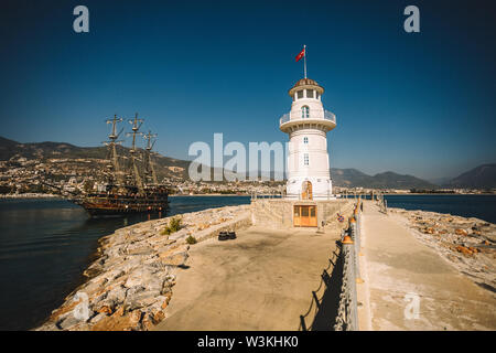 Schön und kleinen weißen Leuchtturm im Hafen von Alanya mit großen alten Schiff im Hintergrund, Türkei, Antalya, Bezirk Stockfoto