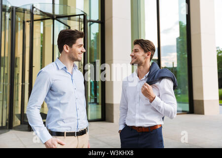 Foto eines Jungen lächelnd zwei Kollegen Unternehmer gehen draußen auf der Straße miteinander reden. Stockfoto