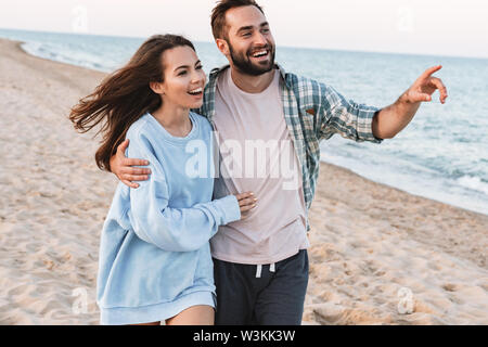 Schöne junge lächelnde Paar Ausgabe Zeit am Strand, Wandern, Umarmung, Zeigefinger entfernt Stockfoto