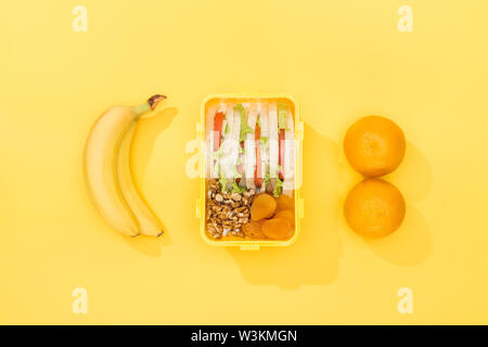 Blick von oben auf die Nüsse, getrocknete Aprikosen mit Sandwiches in Lunch Box in der Nähe von Bananen und Orangen Stockfoto