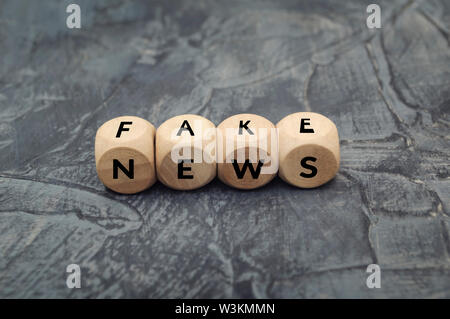 Holzwürfel mit Word gefälschte Nachrichten auf dunklem Hintergrund. Propaganda und Desinformation. Medien und Internet Konzept. Stockfoto