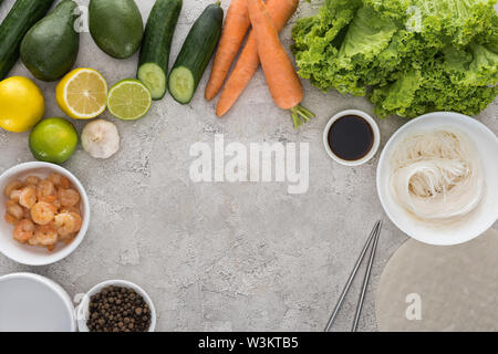 Blick von oben auf die Zitronen, Limetten, Avocados, Karotten, schwarzer Pfeffer, Garnelen, Sojasauce, Reispapier, Knoblauch, Nudeln und Salat auf Tabelle Stockfoto
