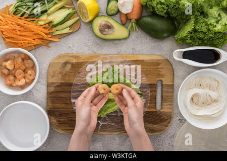 Blick von oben auf die Frau die Garnelen an Salat, auf Schneidebrett Stockfoto