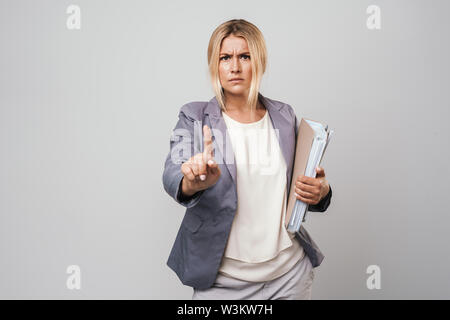 Attraktive verwirrt Blonde wütend Geschäftsfrau tragen Jacke stehend über grauen Hintergrund isoliert, Ordner, Stockfoto