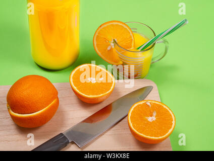 Glas frisch gepresster Orangensaft mit frischen Früchten auf grünem Hintergrund Stockfoto