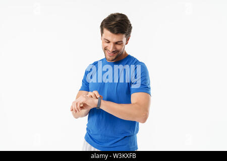 Fotos von lächelnden hübscher junger Sport Fitness Mann stehend über weiße Wand mit watch Uhr Hintergrund isoliert. Stockfoto