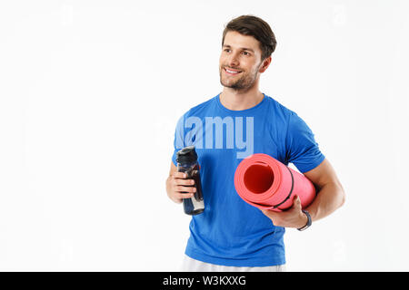 Foto von athletischer Mann mit casual t-shirt Lächeln beim Tragen Fitness Matte und Wasserflasche auf weißem Hintergrund Stockfoto
