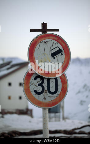 Zwei alte schmutzige Verbotszeichen Verkehrsschild: überholverbot oder vorbei und die Geschwindigkeitsbegrenzung. Haus und Snowy Mountains in Abend im Hintergrund. Stockfoto