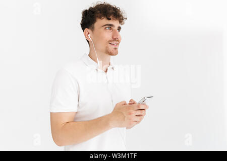 Foto closeup der kaukasischen curly Mann in casual t-shirt lächelnd, während Sie Ohrhörer und Holding Smartphone auf weißem Hintergrund Stockfoto