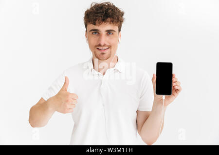 Foto Nahaufnahme von gutaussehenden Mann im casual t-shirt, Daumen oben gedrückt und der Bildschirm des Smartphones an Kamera auf weißem Hintergrund Stockfoto