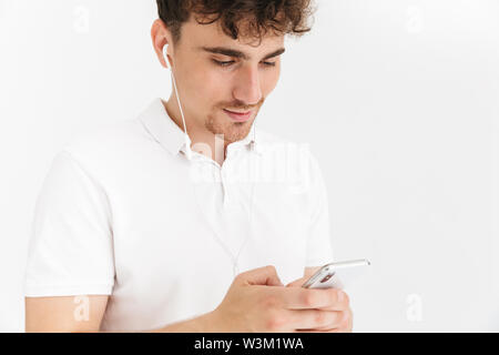 Foto closeup Junger curly Mann in casual t-shirt mit Ohrhörer und Holding Smartphone auf weißem Hintergrund Stockfoto