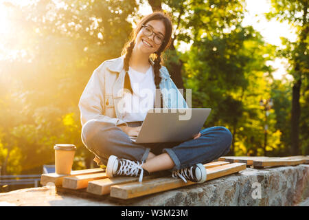 Bild der kaukasischen jugendlicher Mädchen tragen Brillen mit Laptop sitzend auf Bank mit Kaffee zum Mitnehmen im Green Park Stockfoto