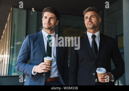 Bild von ihnen Unternehmer Partner in Anzug trinken Kaffee zum Mitnehmen, während außerhalb Office Center gekleidet Stockfoto