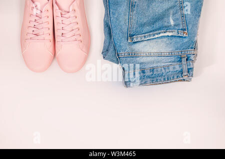 Flache Komposition mit einer Reihe von Kleidung, Jeans und rosa Turnschuhe. Ansicht von oben auf einem weißen Hintergrund. Flach, Ansicht von oben Stockfoto
