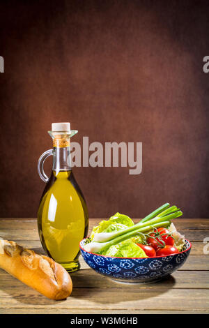 Hochwertiges Olivenöl Extra Vergine aus Jaen, Spanien, in einer dekorativen Flasche mit den Voraussetzungen eines gemischten Salat und ein Baguette Brot Stockfoto