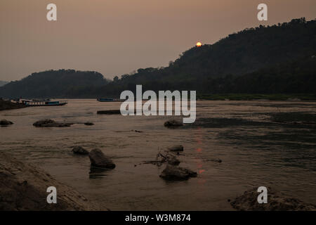 Blick auf einige Flusskreuzfahrtschiffe auf dem Mekong und Chomphet Bezirk über den Fluss in Luang Prabang, Laos, bei Sonnenuntergang. Stockfoto