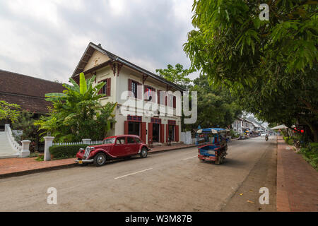 Alte Citroen Auto vor einer alten französischen Kolonialgebäude und wenig Verkehr auf der idyllischen Sakkaline Straße in Luang Prabang am Morgen geparkt. Stockfoto