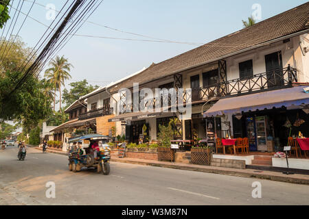 Fahrrad, Roller, Autos und zwei farbenfrohe Dreirad Taxi genannt Jumbo (oder Tuk Tuk) auf dem Khem Khong Straße in Luang Prabang, Laos an einem sonnigen Morgen Stockfoto