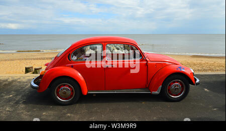 Classic Red Volkswagen Käfer an der Strandpromenade mit Blick aufs Meer und den Strand im Hintergrund geparkt. Stockfoto