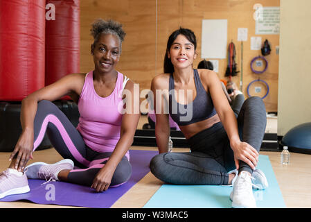 Lächelnde Frauen sitzen auf Yoga-Matten Stockfoto