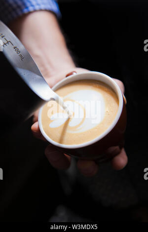 Barista gießen Milch in Kaffee Stockfoto