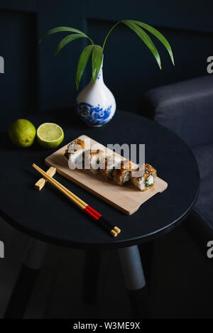 Sushi am Tisch mit Stäbchen, Vase und Kalk Stockfoto