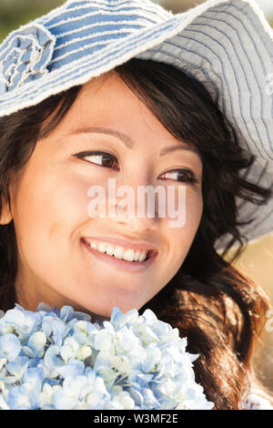 Schön, glücklich, gesund, Lächeln, junge asiatische Frau mit weiche, glatte, makellose Haut im Freien im Sommer. Sie hält frische Blumen und das Tragen eines Stockfoto