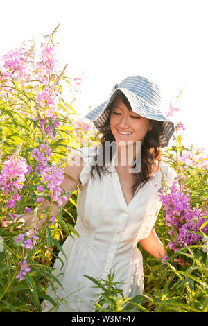 Schön, glücklich, gesund, Lächeln, junge asiatische Frau Blumen pflücken im Freien im Sommer. Sie trägt ein feminines Kleid und Sonnenhut. Natürliche Gesundheit Stockfoto