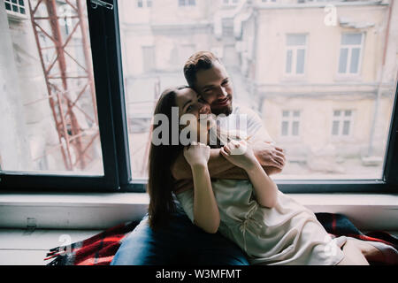 Junges Paar Umarmung durch Wohnung Fenster Stockfoto