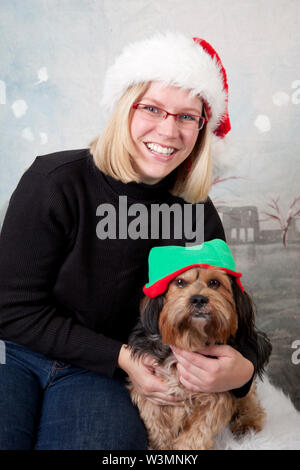 Eine blonde Frau in einem Santa hat und eine niedliche braune Hund in ein Elf hat Posieren im Studio Stockfoto