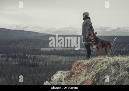 Eine junge Frau ist, geniessen Sie die Aussicht über das Land zusammen mit ihrem Hund. Yukon Territory, Kanada Stockfoto