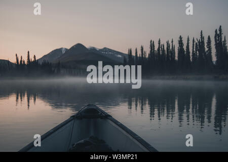 Ein Kanu gleitet über die ruhigen Wasser eines Flusses während der Himmel glüht leise beginnt, kurz vor dem Sonnenaufgang. Yukon Territory, Kanada Stockfoto