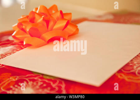 Red Geschenkpapier auf ein Feld mit einem orangefarbenen Pfeil und Bogen einen Umschlag mit der Kopie Raum Stockfoto