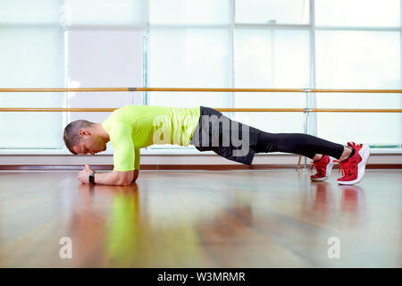 Es Plank zuversichtlich muskulösen jungen Mann mit Sport Verschleiß und tun Ganzkörperstütz während des Trainings auf dem Boden im Loft Innenraum Stockfoto