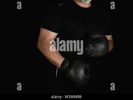 Junge Mann steht in einem Rack, das Tragen von sehr alten Vintage Schwarze Boxhandschuhe auf seinen Händen, dunklen Hintergrund Stockfoto