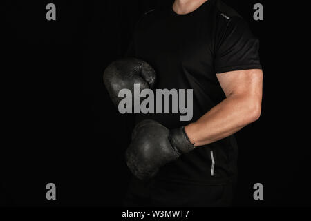 Junge Mann steht in einem Rack, das Tragen von sehr alten Vintage Schwarze Boxhandschuhe auf seinen Händen, dunklen Hintergrund Stockfoto