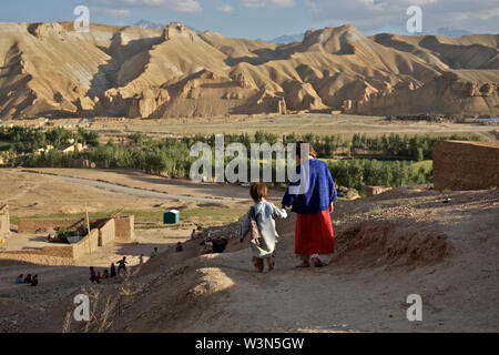 Aqila, 8, führt sie 18 Monate alten Bruder, Abdul Wahid, den Hügel hinunter, auf andere Kinder, die spielen, in der Ortschaft Ragshad, in der zentralen Provinz Bamyan. Ihr Vater arbeitet als Hilfsarbeiter und die sieben Kinder der Familie dürfen bis zu acht Stunden pro Tag Teppiche weben neben der Teilnahme an der Schule arbeiten. Es dauert zwei Monate für die Familie ein 5 Quadratmeter Teppich, Wert 800 Afghanen zu machen, ÜBER UNS $ 24. Das Haus hat kein fließendes Wasser oder Gas, so dass die älteren Jungs zwei Stunden täglich Wasser aus einem Datenstrom für lokale Aufzeichnung und Brennholz aus den Bergen zu sammeln. Ragshad, Provinz Bamyan, Af Stockfoto