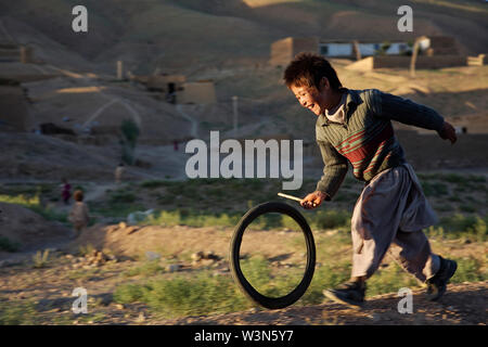 Eine lachende Junge jagt ein Fahrrad Schlauch mit einem Stock, in der Ortschaft Ragshad, am Stadtrand von Bamian Stadt in der zentralen Provinz Bamyan. Er ist Mitglied der ethnischen Minderheit der Hazara. Juli 4, 2007. Stockfoto