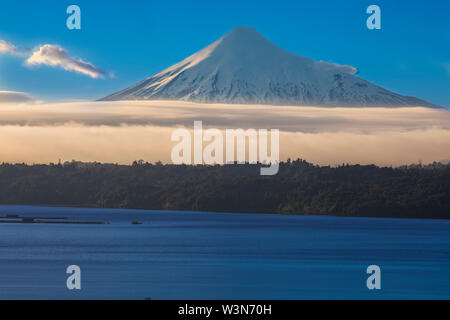 Die erstaunliche schneebedeckten Vulkan Osorno Gipfel über dem Wasser und Wolken von Rupanco See, die Bäume im Wald und die Wolken ein beeindruckender Landschaft Stockfoto