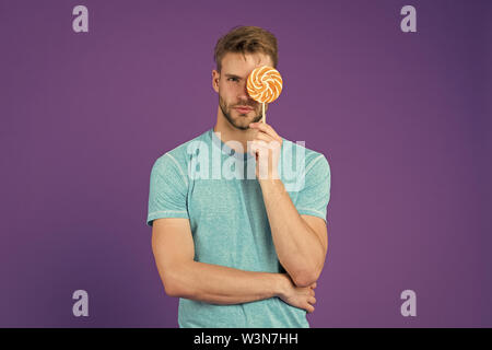 Mann mit Borsten mag Lollipop. Cheat meal Konzept. Zucker schädlich für die Gesundheit. Kerl halten Lollipop candy violett unterlegt. Geschmack der Kindheit. Lollipop Spaß. Mann essen großen bunten süßen Lutscher. Stockfoto