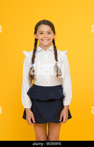 Smart cutie. Süße kleine Mädchen lächelnd auf gelben Hintergrund. Gerne kleine Mädchen tragen Schuluniform. Grundschule Mädchen mit geflochtenem Haar in langen Zöpfen. Adorable girl Stolz, ein Schüler. Stockfoto