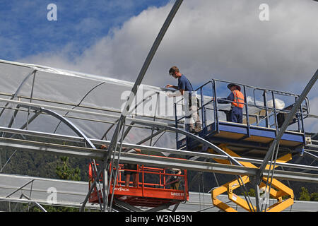 Greymouth, Neuseeland, 12. Dezember 2018: Handwerker sichern Sie den Kunststoff auf einen neuen Tunnel House. Stockfoto