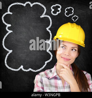 Denken junge weibliche Bauarbeiter, Architekt, Ingenieur, Surveyor tragen, hardhat auf blackboard Denken mit der Hand zum Kinn zum Denken Blase auf schiefertafel Textur. Stockfoto