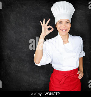 Koch, perfekte Hand unterzeichnen und Menü Tafel. Frau vor leeren Menü Tafel. Happy Köchin, Koch oder Bäcker durch leere Schiefertafel Menü tragen Küchenchef weißen Uniform und Mütze Stockfoto