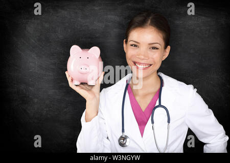 Krankenversicherung und Gesundheitsversorgung geld Konzept. Ärztin Frau mit Übersicht Sparschwein Lächeln glücklich, dass Einsparungen. Junge Mediziner Arzt auf blackboard Hintergrund. Stockfoto